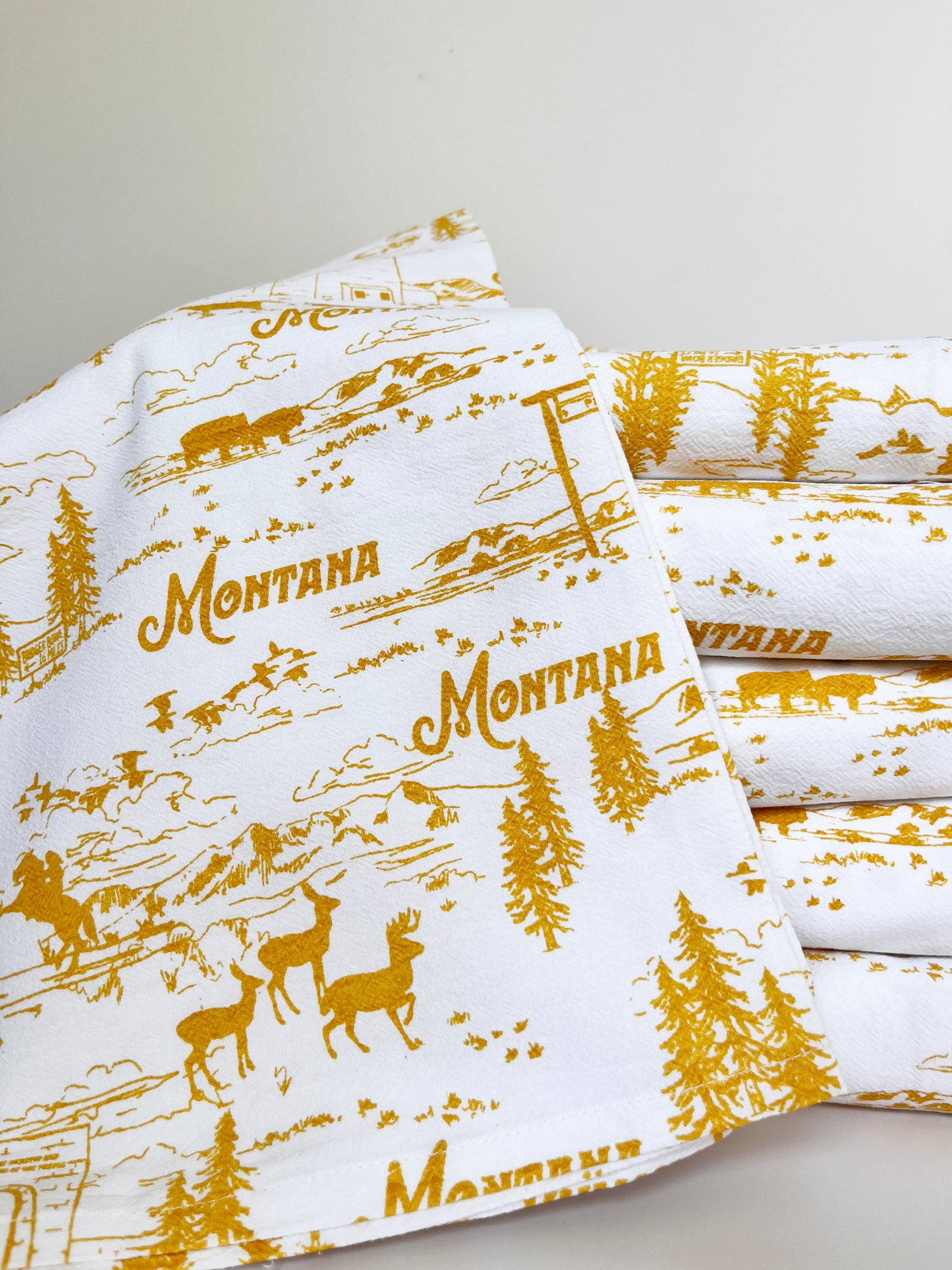 cute cotton tea towel with montana scenes hand drawn illustrations yellow ochre screen print elk bison pine trees ski lift bridger bowl mountains birds roosevelt arch yellowstone glacier national park fun montana souvenir coin laundry cotton kitchen towels