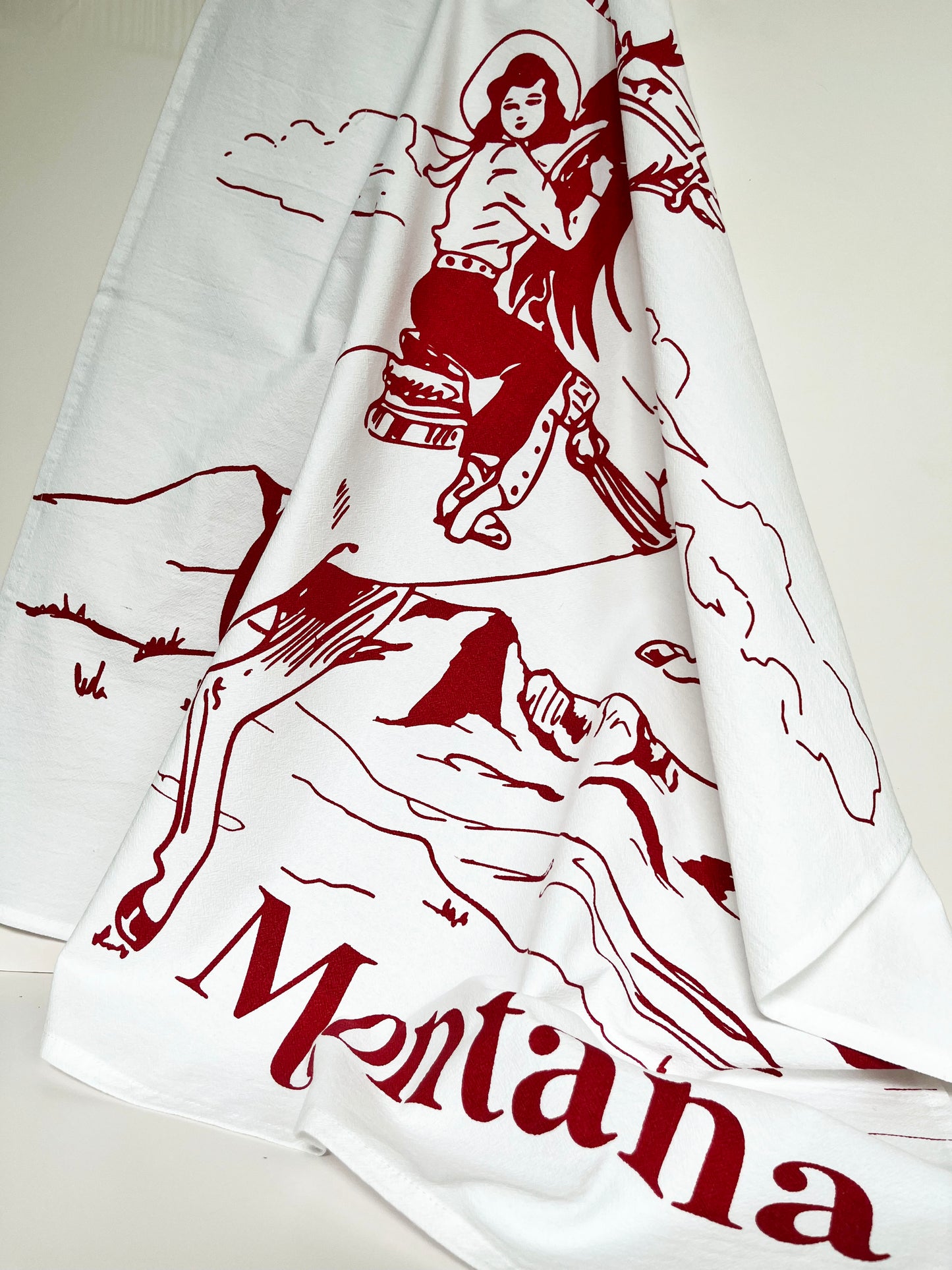 cotton kitchen towel hand drawn illustration western cow girl cowgirl riding bucking horse red mountains plains big sky text says there's no place like montana coin laundry tea towels