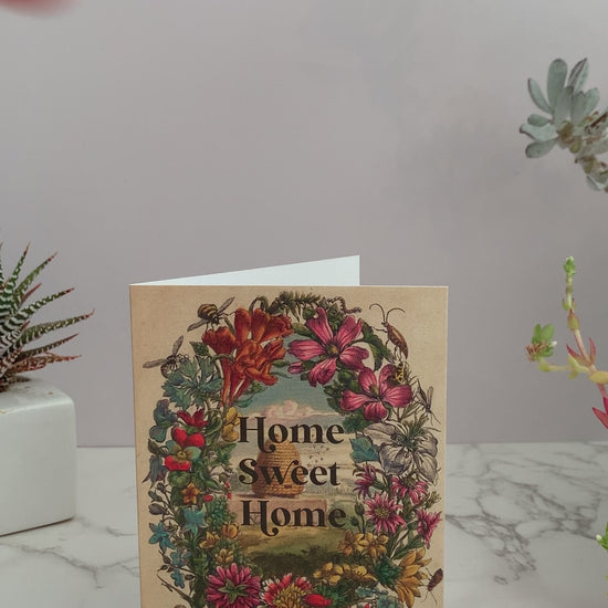 Perfect greeting card for a house warming, a move, or congratulations on purchasing a new home. Vintage image featuring a beehive surrounded by a floral frame and bees. Greeting says, "Home Sweet Home." Color pallet is vintage colors of pinks, reds, blues, greens, and yellows. Blank inside.