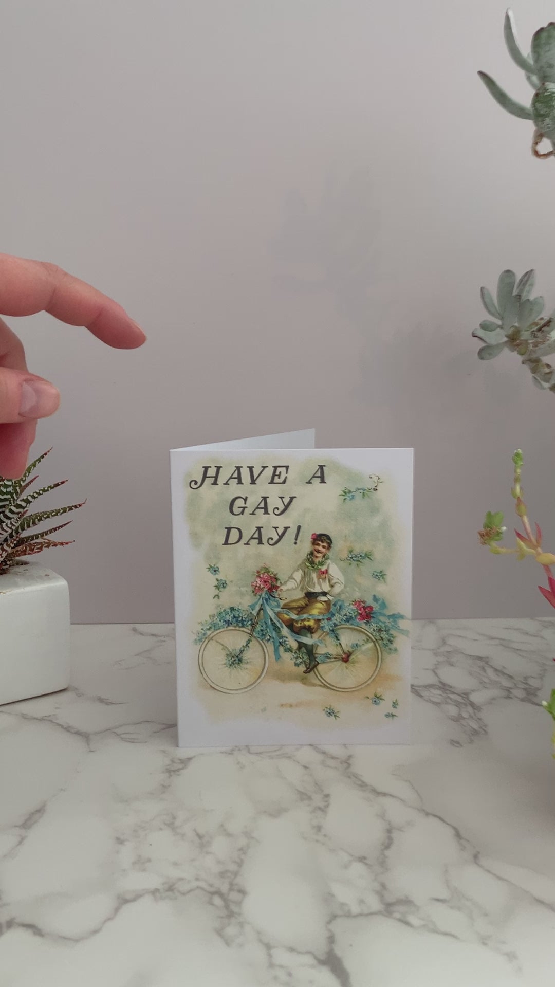 All purpose greeting card that says "Have a gay day!" on the front. Vintage image featuring a happy man with a mustache on a bicycle, with flowers and ribbons. Color pallet is yellows and blues with a little pink. Blank inside.