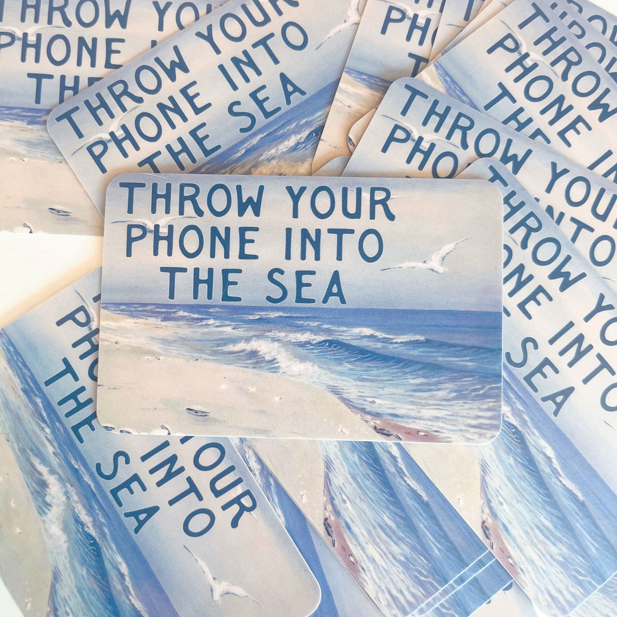 A pile of rectangular stickers featuring a blue ocean wave design and the phrase “THROW YOUR PHONE INTO THE SEA” in dark blue text.