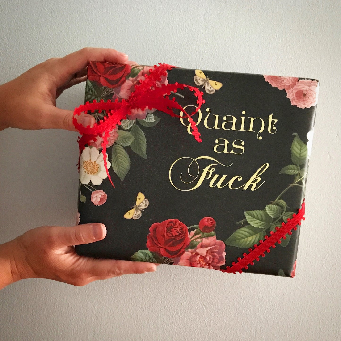 single sheet of wrapping paper black background with floral design red pink roses white flowers butterfly says quaint as fuck af coin laundry