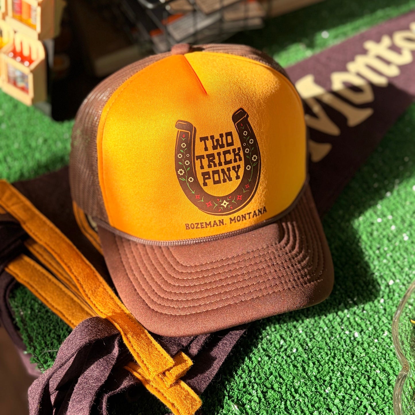 Yellow and brown cap with 'Two Trick Pony' logo on a green surface