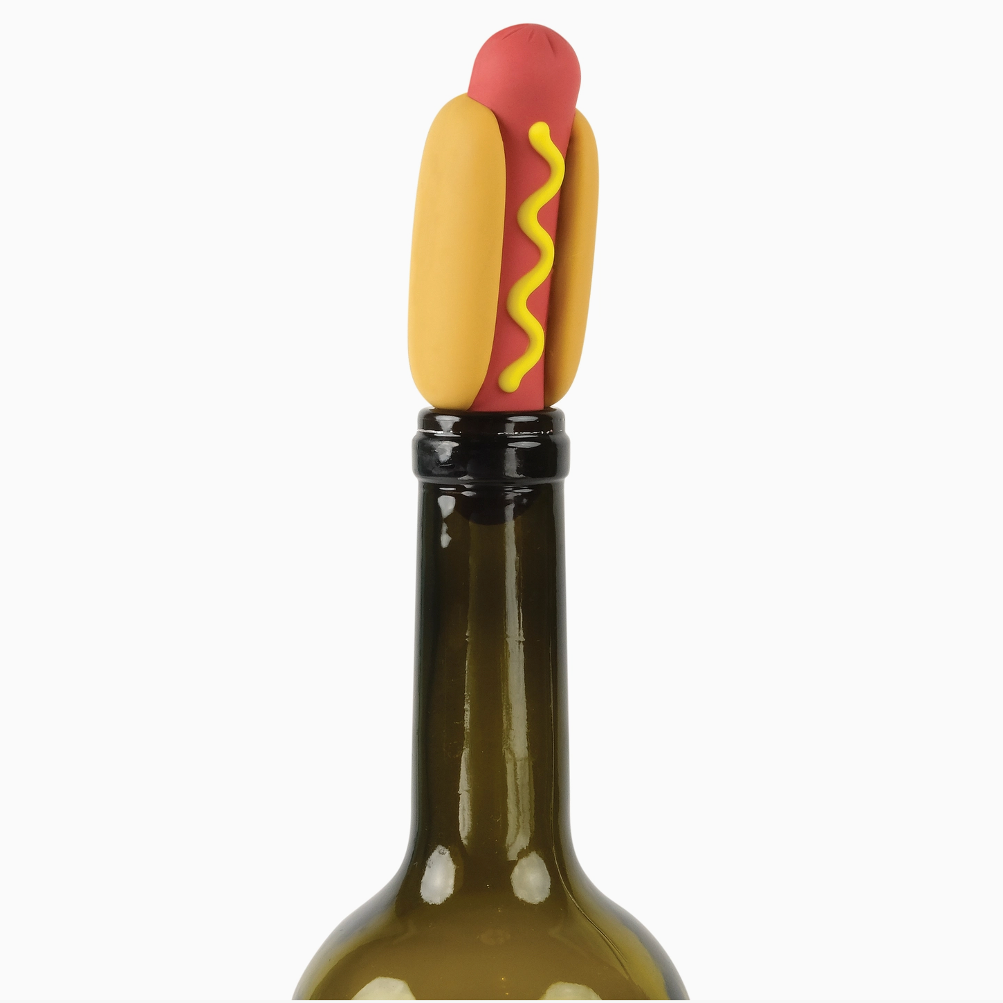 A novelty bottle stopper shaped like a hot dog in a bun, with a red sausage, yellow mustard, and tan bun, shown inserted into the neck of a dark glass bottle against a white background.