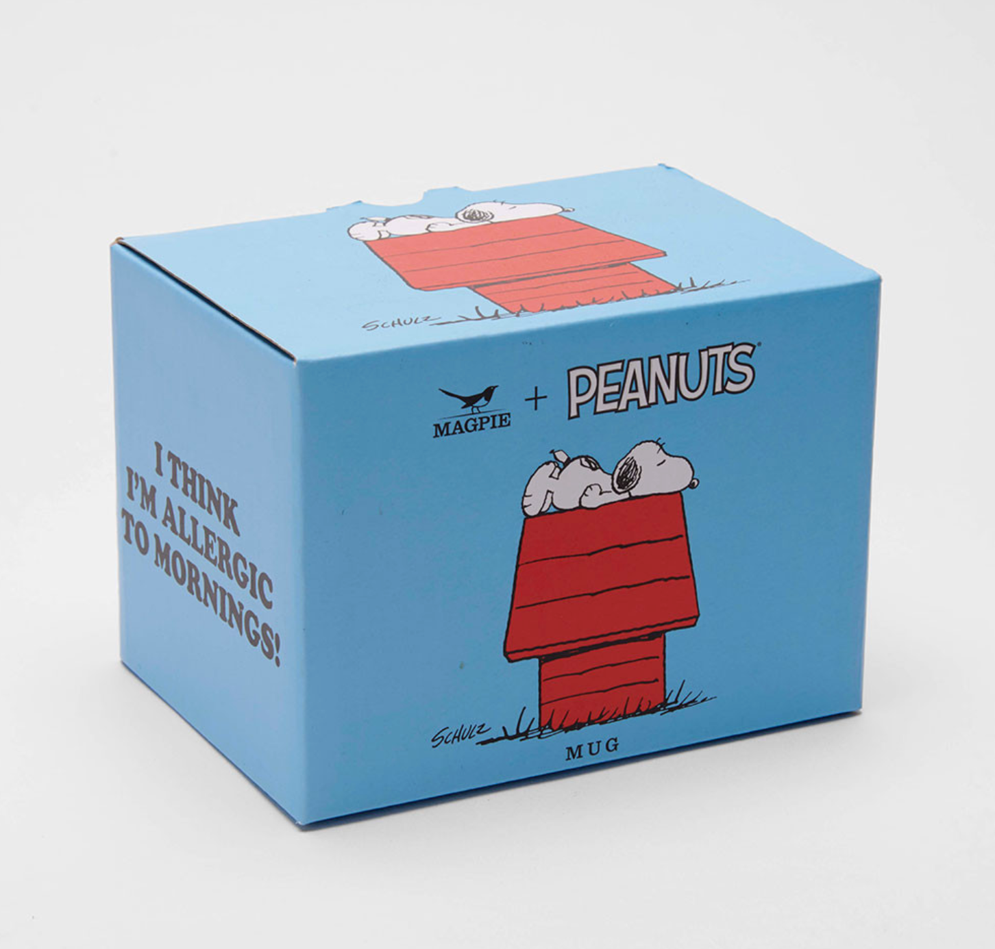 A light blue ceramic mug shaped like a Peanuts-themed box, featuring Snoopy and Woodstock sleeping in a red doghouse, with the text 'I THINK I'M ALLERGIC TO MORNINGS!' and 'MAGPIE + PEANUTS'.