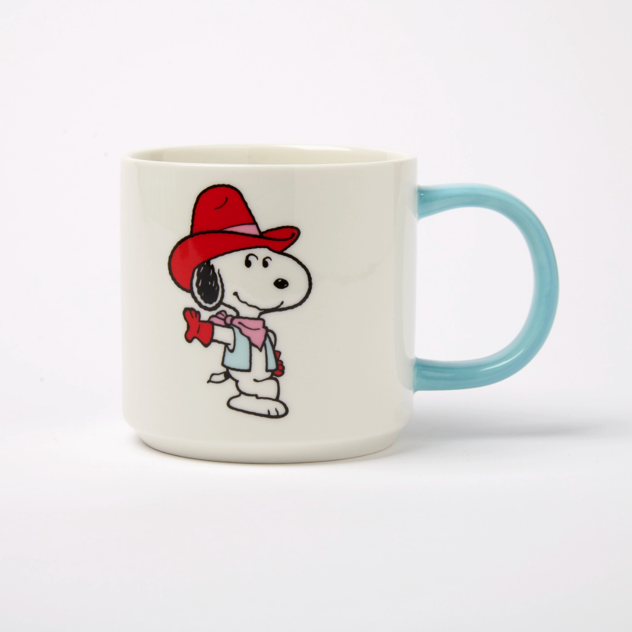 A ceramic coffee mug featuring the Peanuts character Snoopy wearing a red cowboy hat and pink scarf, with a light blue handle on a white background.