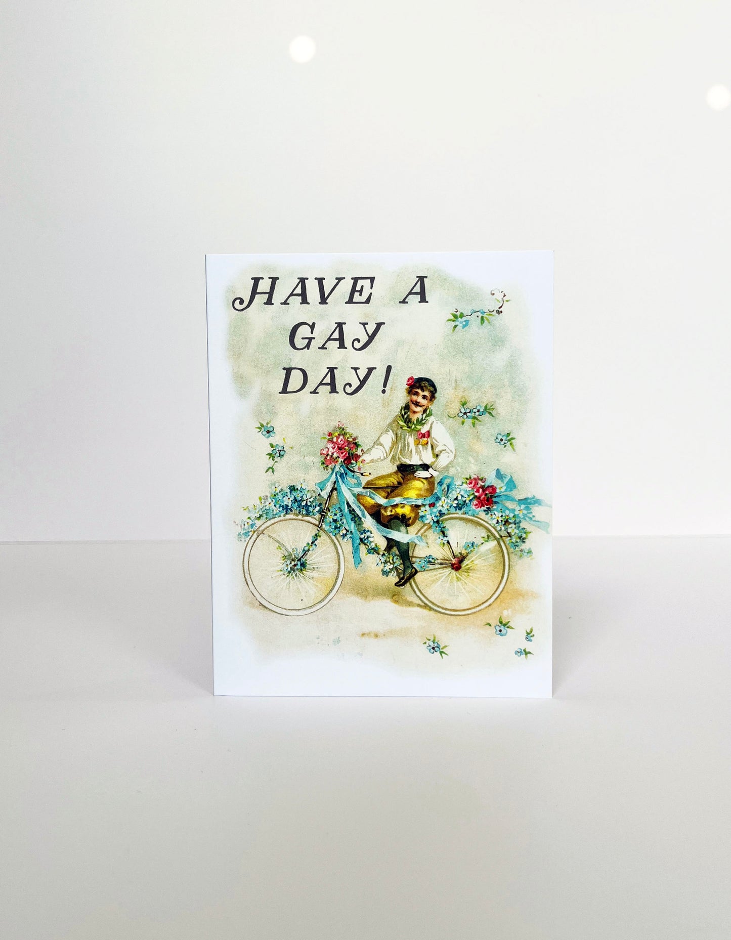 victorian style man with mustache on bicycle with blue pink flowers ribbons greeting card text have a gay day retro vintage style blank inside joyous fun celebratory exciting lgbtq playful bold coin laundry 