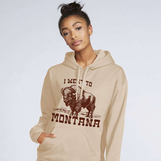 Person wearing a beige hoodie with a graphic of a bison and text I went to Montana on a plain background