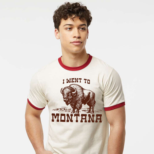 Person wearing a white ringer t-shirt with red trim featuring a bison graphic and text on a plain background