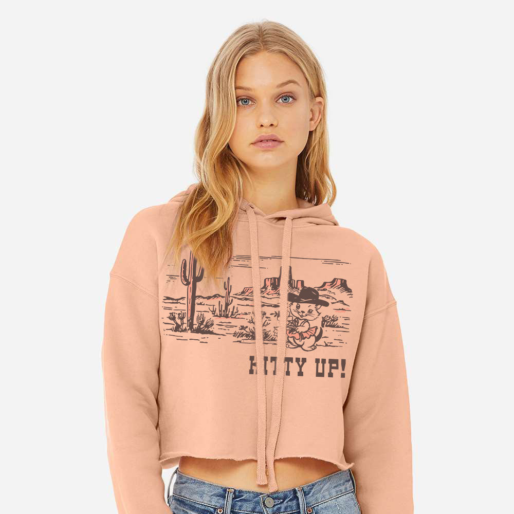 Woman wearing a pink hoodie with graphic design and text, standing against a white background