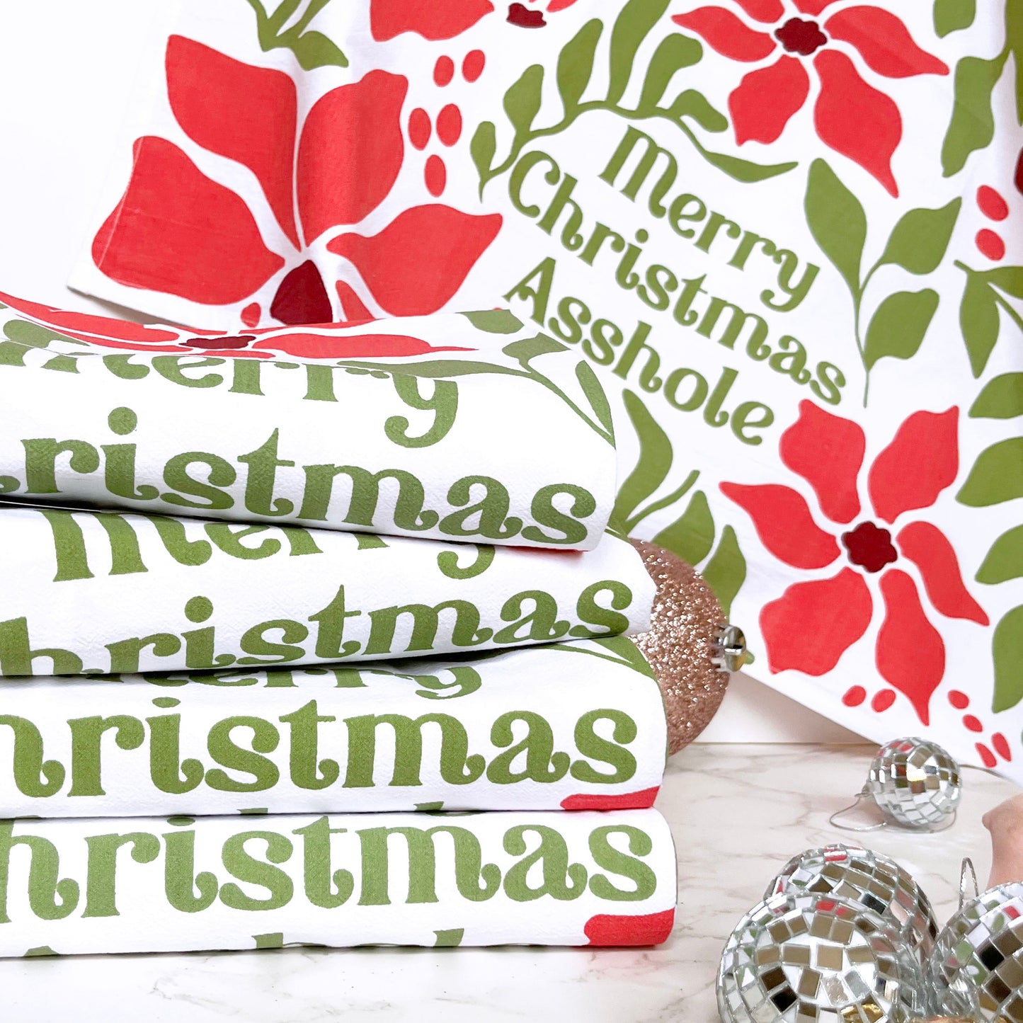 Stack of Christmas-themed towels with poinsettias and 'Merry Christmas Asshole' text on a decorative background.