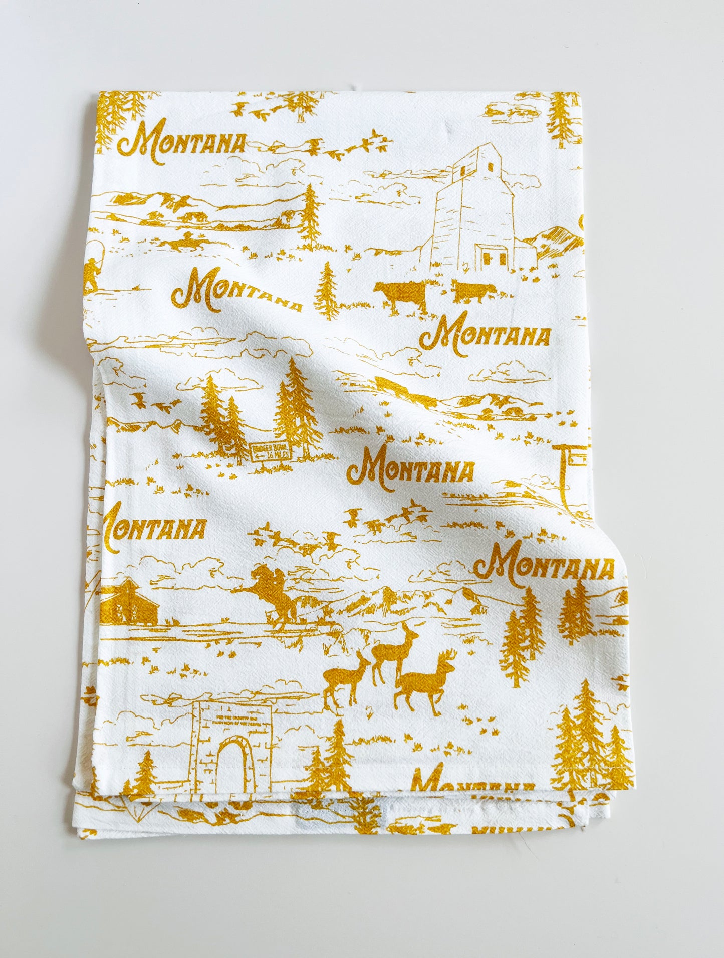 montana theme cotton kitchen towel dish towel with scenes from montana pine trees bison elk mountains yellowstone national park glacier ranch grain elevator yellow ochre screen print on white towel coin laundry montana fun travel gift