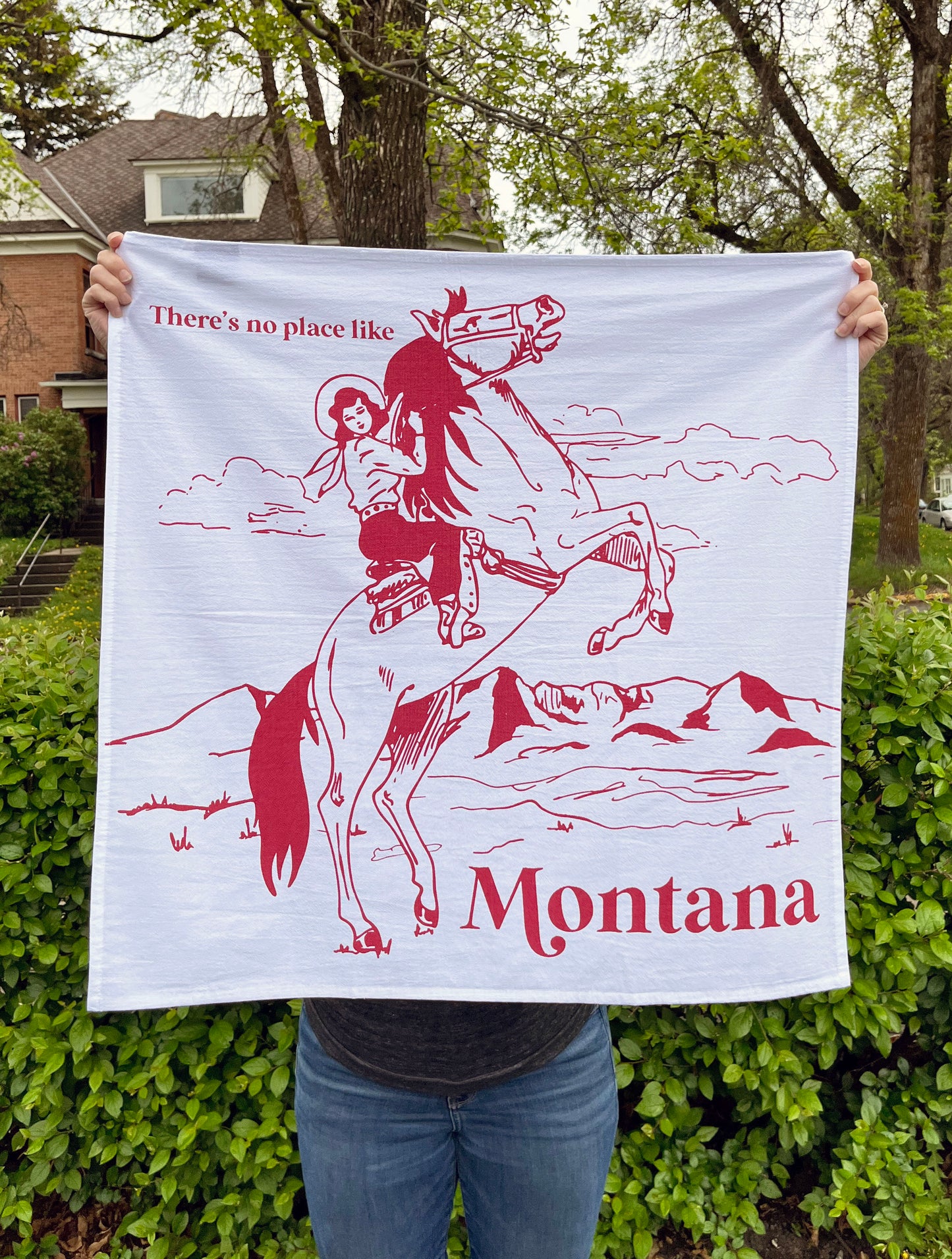 all over screen print on cotton dish towel theres no place like montana cowgirl riding bucking bronco horse red print fun gifts and souvenirs coin laundry montana  