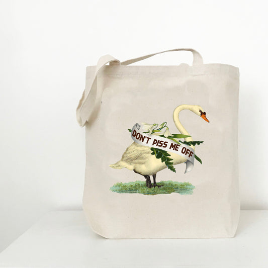 A natural canvas tote bag with a printed graphic of a white swan carrying a banner that reads 'DON'T PISS ME OFF' on a white background.