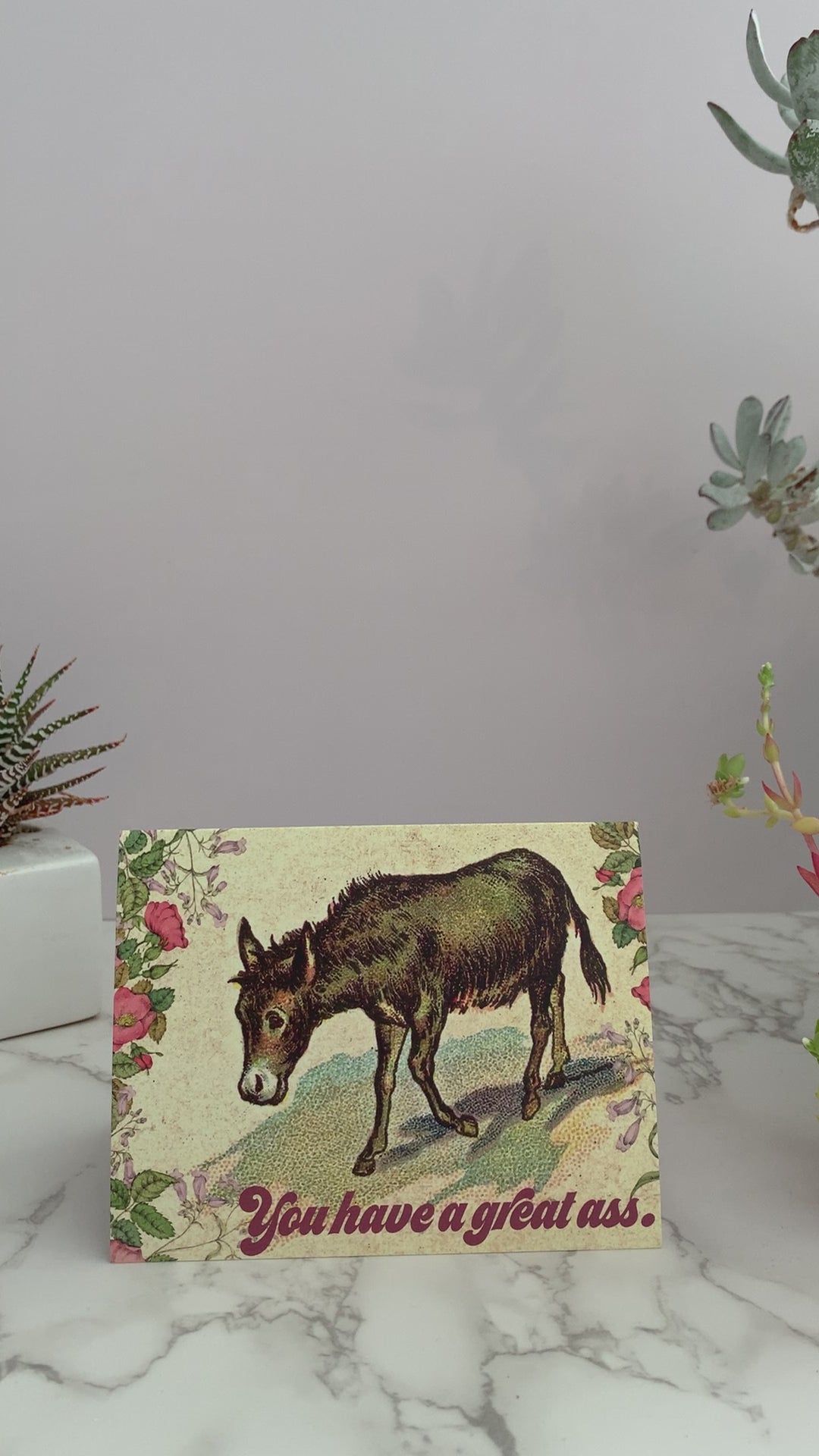 Greeting card perfect to send to your crush, your husband, your wife, your best friend, Valentine's day, or any occasion. Featuring an image of a brown vintage donkey surrounded by flowers. Color pallet is yellows, pinks, greens and blues. Greeting says, "You have a great ass." on the front. Blank inside.