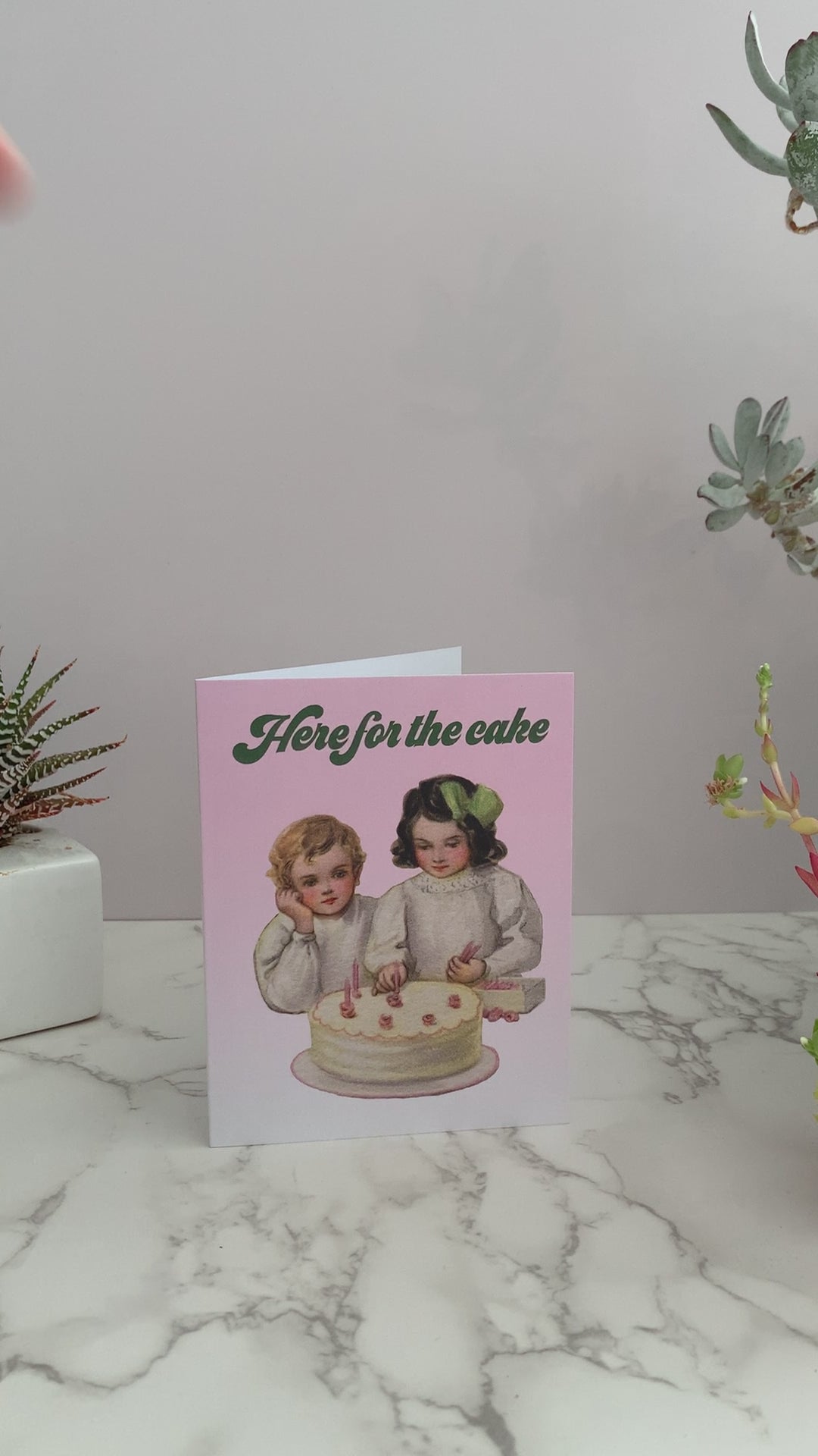 All purpose greeting card. Can be used for celebrations, birthdays, weddings, anniversaries, or anything. Front of the card is light pink, with a vintage image of two children putting candles on a cake. Greeting says, "Here for the cake." Inside is blank.