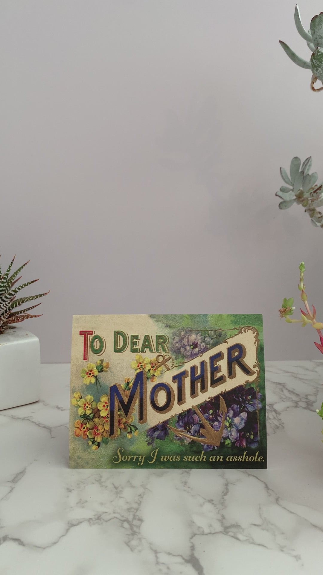 Greeting card with green and yellow background and yellow and purple flowers. Greeting says, "To Dear Mother. Sorry I was such an asshole." Blank inside.