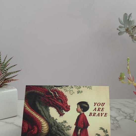 All purpose greeting card that says "You are Brave" on the front. Vintage images featuring a little boy calmly  staring into the face of a large red dragon, next to a tree. Color pallet is reds, yellows, and greens. Blank inside. Perfect to send to a friend who is going through a big life change.