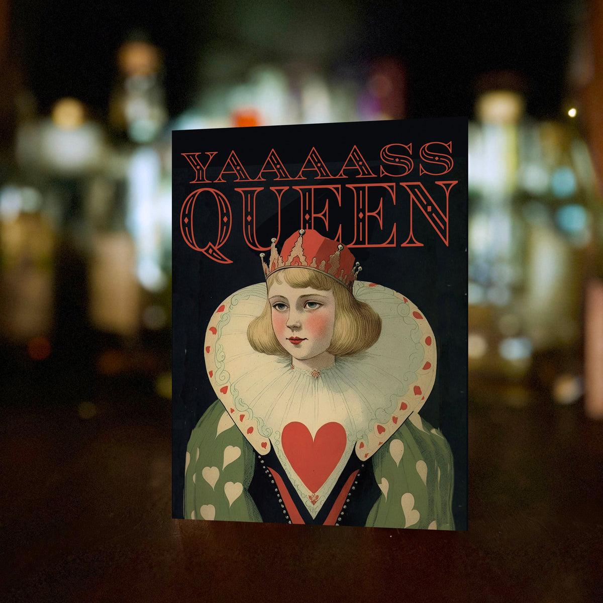 A rectangular card featuring a stylized Queen card illustration with the text 'YAAAASS QUEEN' in red, standing upright against a dark blurred background.