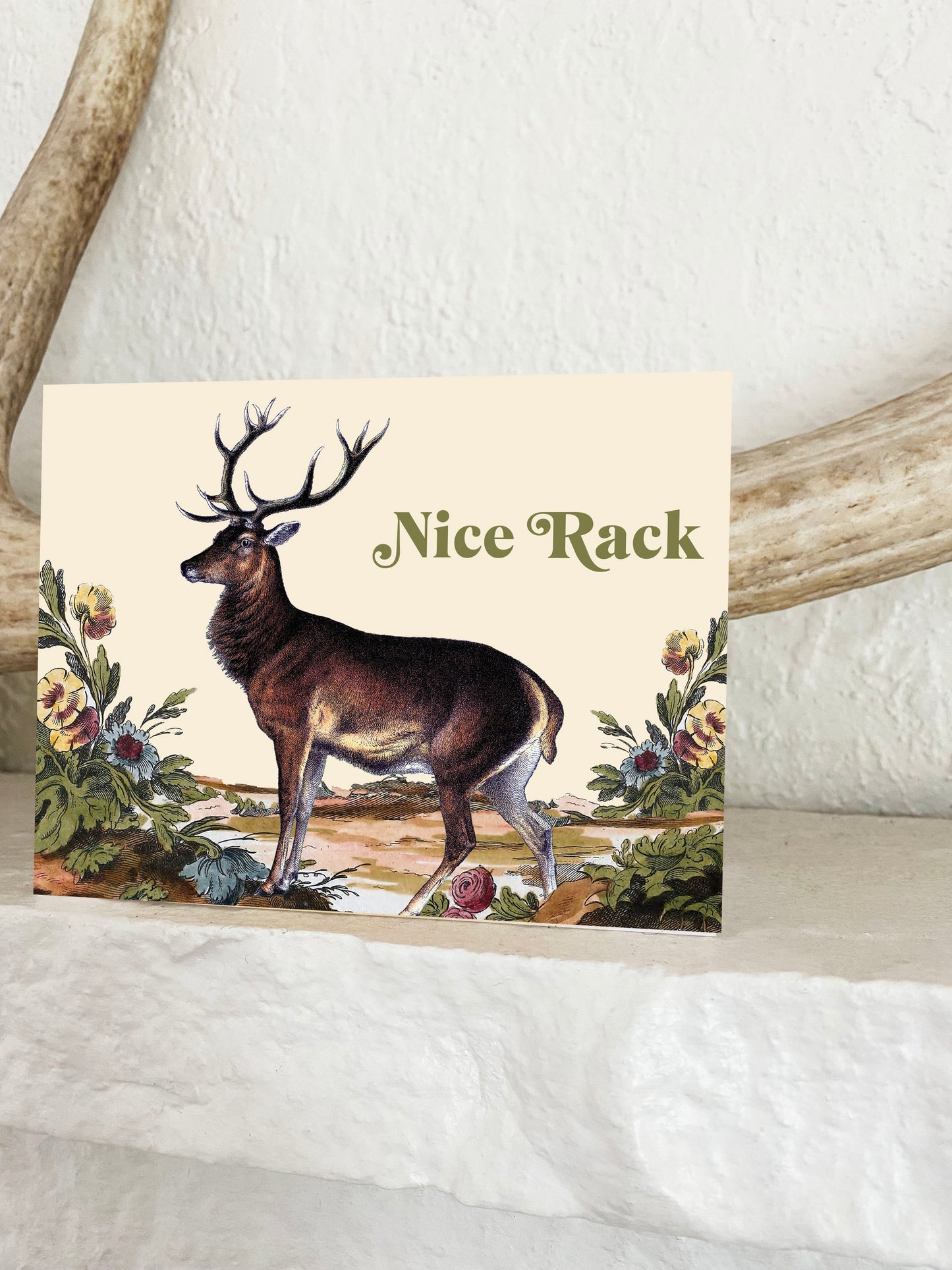 Vintage illustration of deer with large antlers next to wildflowers with text Nice Rack 